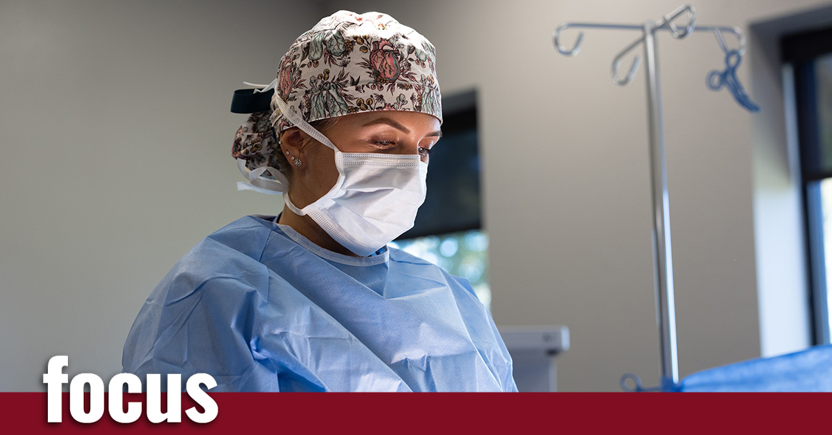 A woman dressed in hospital scrubs and a mask standing in a surgical room