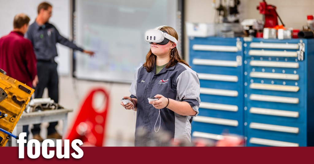 A woman wearing goggles stands in the foreground with two men and a toolbox in the background