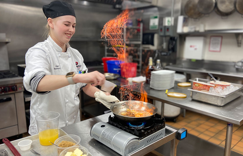 FVTC culinary student flambéing food in a pan over table side burner