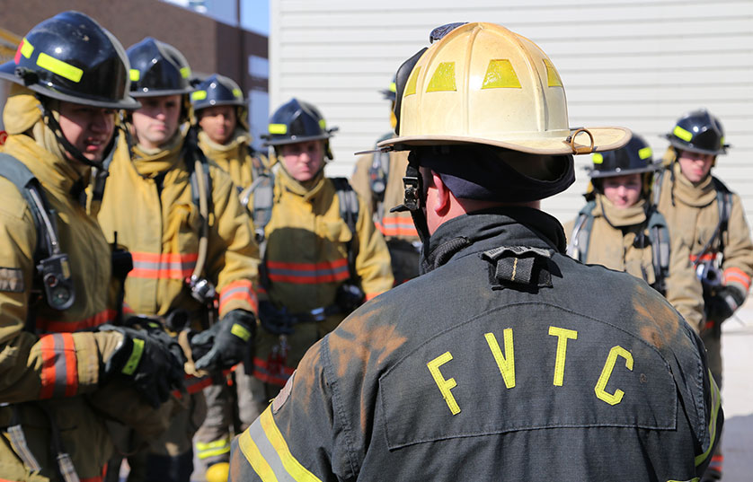 firefighters in firefighter gear standing in group with one firefighter wearing jacket with FVTC on back