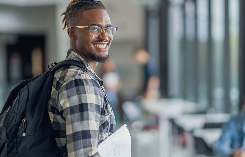 student with backpack on carrying notebook looking back at the camera