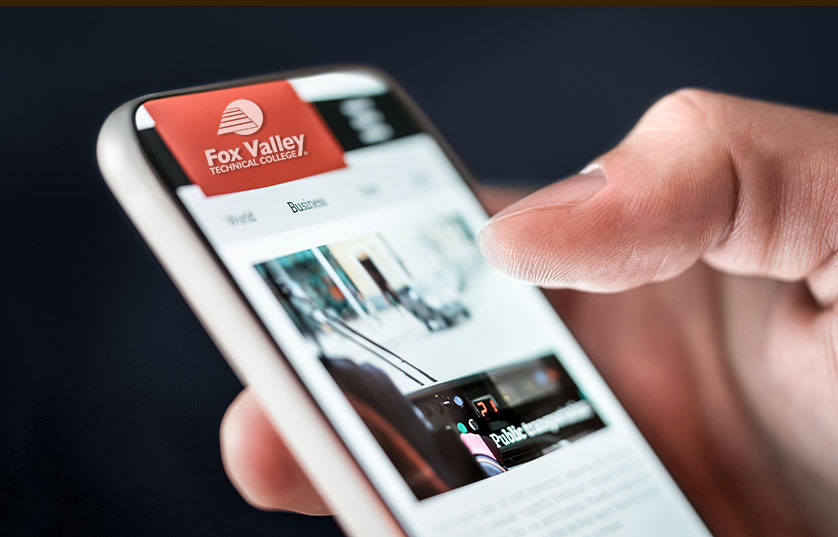 person's hand holding mobile phone scrolling through FVTC news