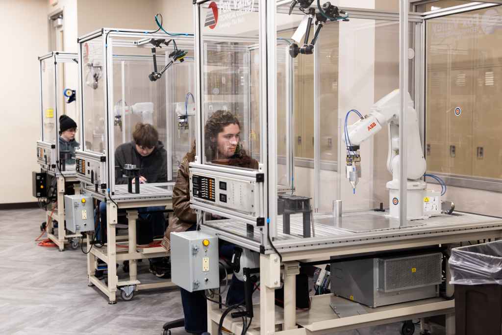 Three FVTC high school automation academy students operate advanced robotic manufacturing equipment in a lab on campus.