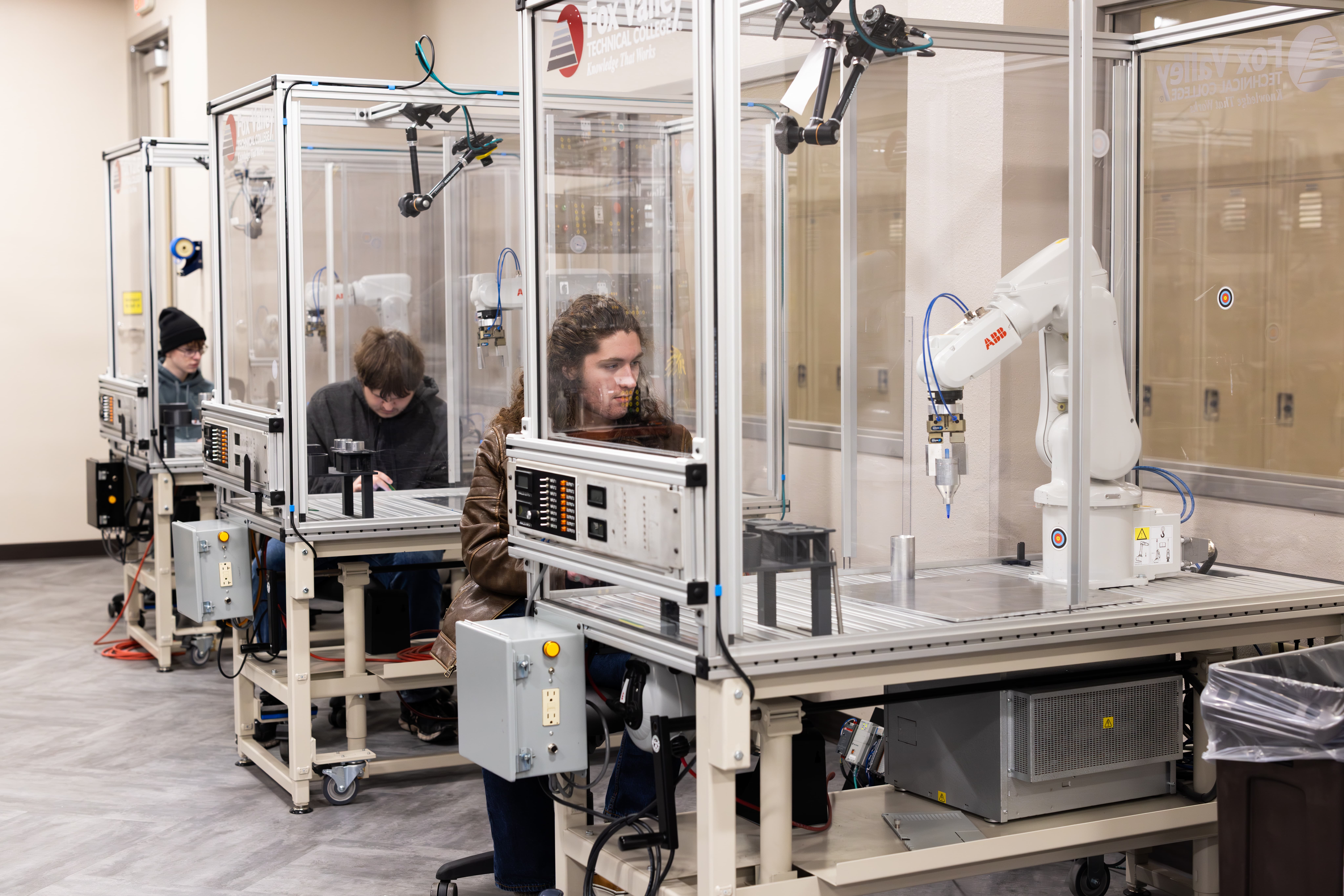 Three FVTC high school automation academy students operate advanced robotic manufacturing equipment in a lab on campus.