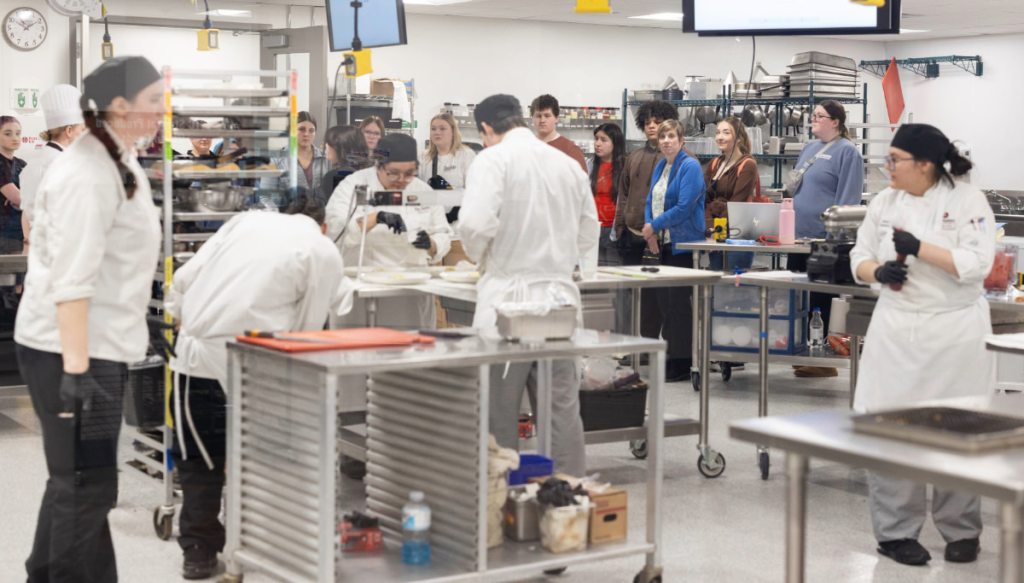 A team of culinary students in a kitchen, focused on cooking and food preparation, highlighting collaboration.