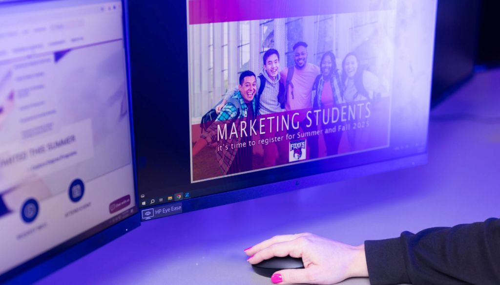 a hand on a mouse with marketing students on screen
