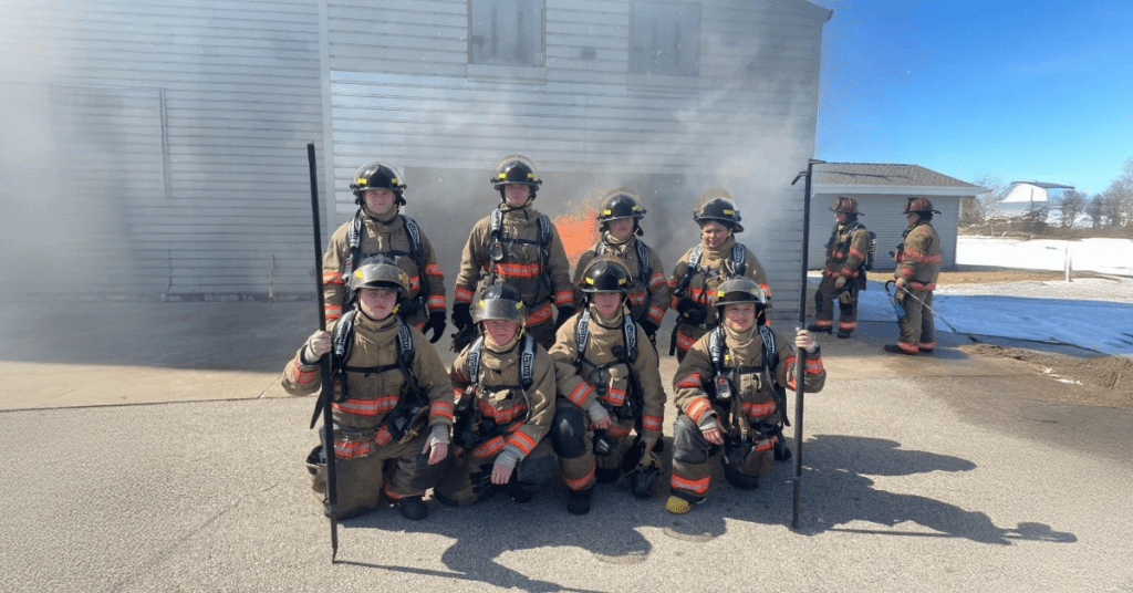 Firefighting students pose outside practice building