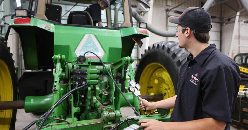A man repairs a tractor inside a garage, surrounded by tools and equipment.