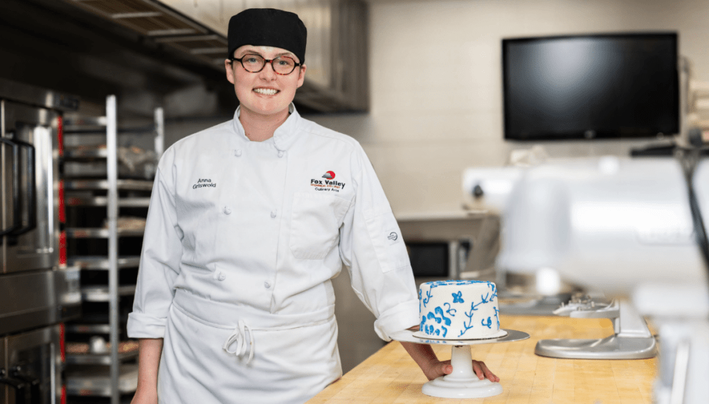 A Baking student in the baking lab posing with a decorative cake.