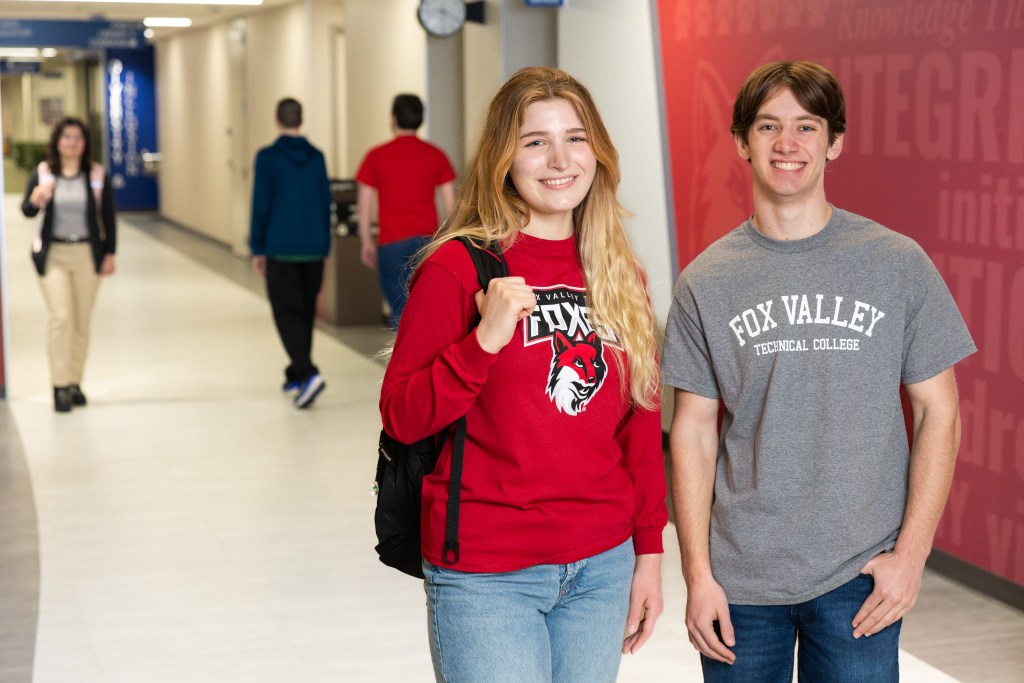 Two students standing in hallway. Other students walking in background.