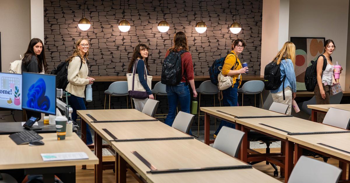 Interior Design students walk in a line through a newly renovated room, past the cafe bar with globe lights.