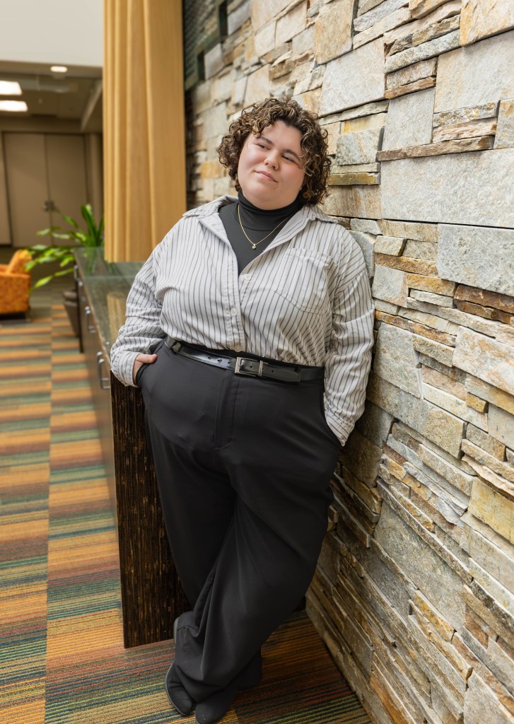 Hailee Boesch stands against a tan stone wall to the right. 