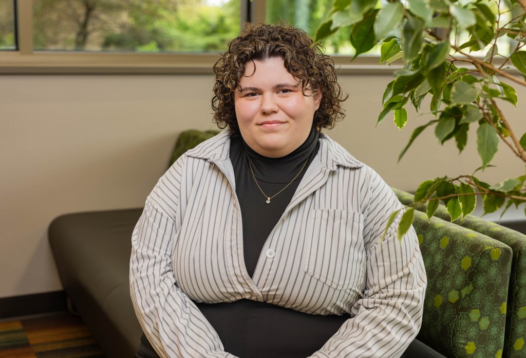 Hailee Boesch sits on a bench, with a green plant on the right. 
