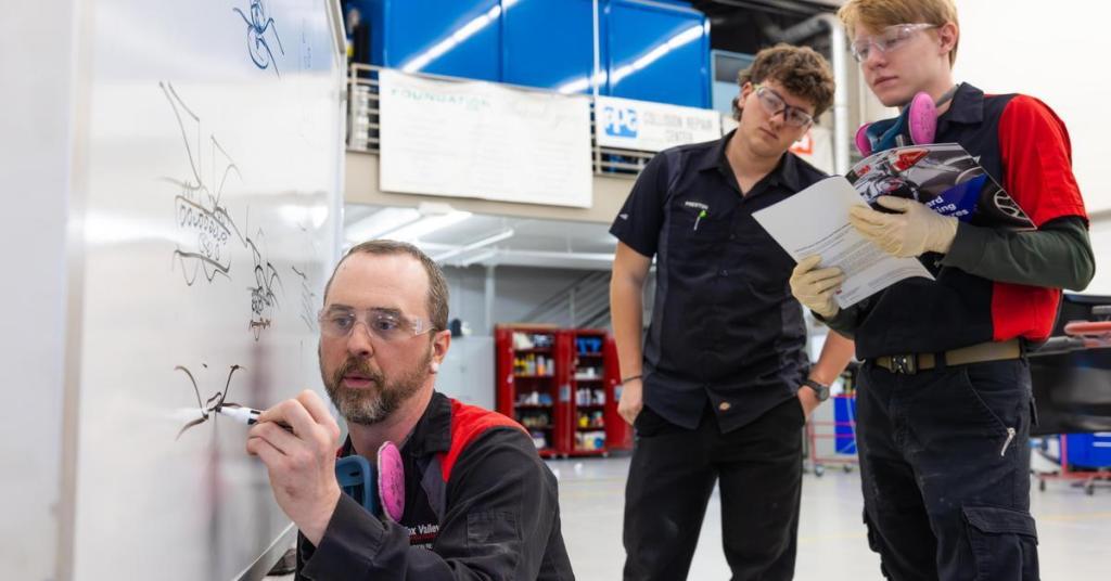 Students and an instructor looking at a whiteboard in an automotive collision repair lab.